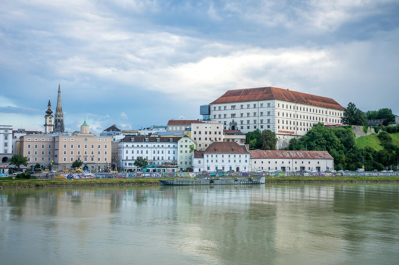 Linz, Rakousko: Panorama města s řekou Dunaj, budovy, kostelní věže a zatažená obloha. Cestování, architektura.