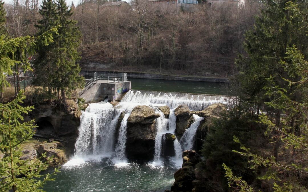 Traunfall, největší vodopád Rakouska. Pohled na kaskády, zeleň a budovy v pozadí. Příroda a vodní síla.