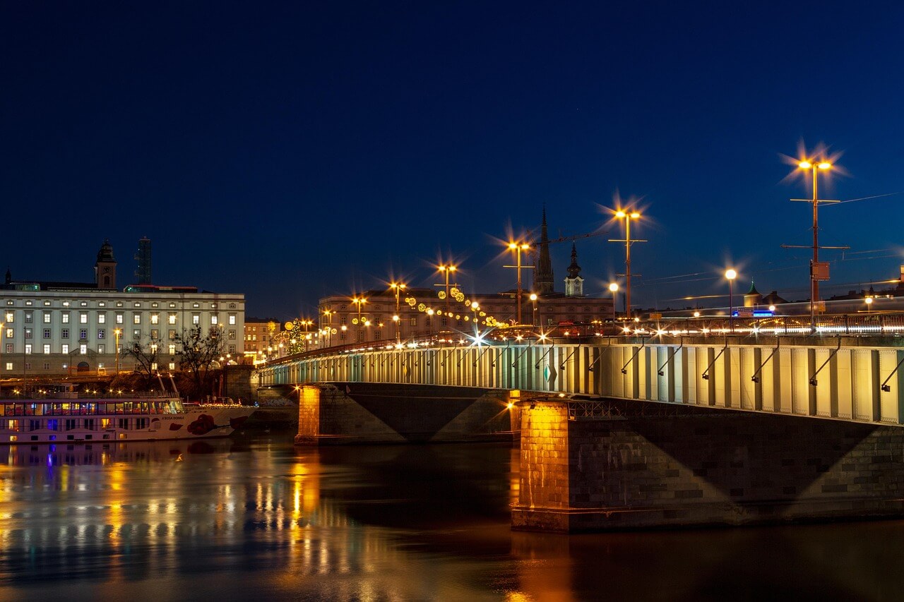 Noční pohled na most přes řeku. Osvětlené budovy a lampy. Městská krajina, noční město Linz.