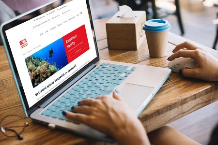 Práce na notebooku. Extrémní sporty zobrazené na obrazovce, káva, dřevěný stůl.