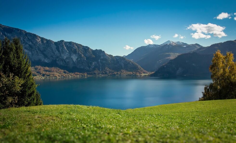 Krásné jezero v Alpách s horami, zelenou trávou a modrou oblohou. Ideální pro turistiku a relaxaci v přírodě.