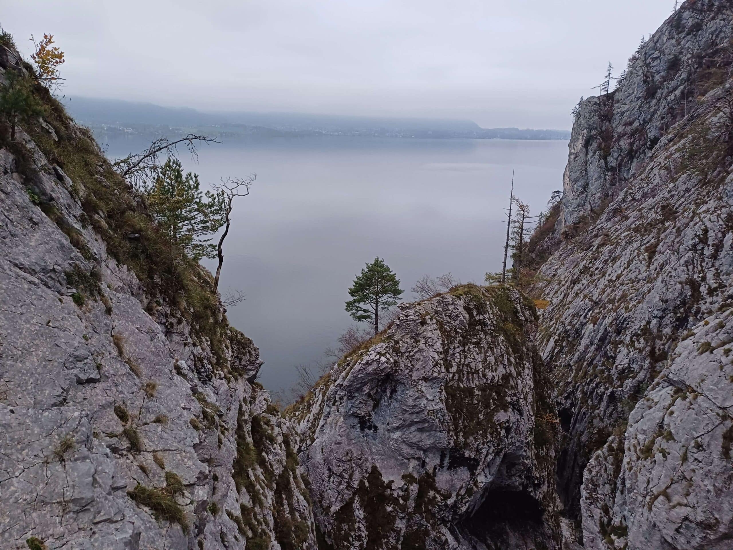 Mlhavý pohled na jezero z úzké skalní soutěsky. Skály, stromy, příroda, turistika a scenérie.