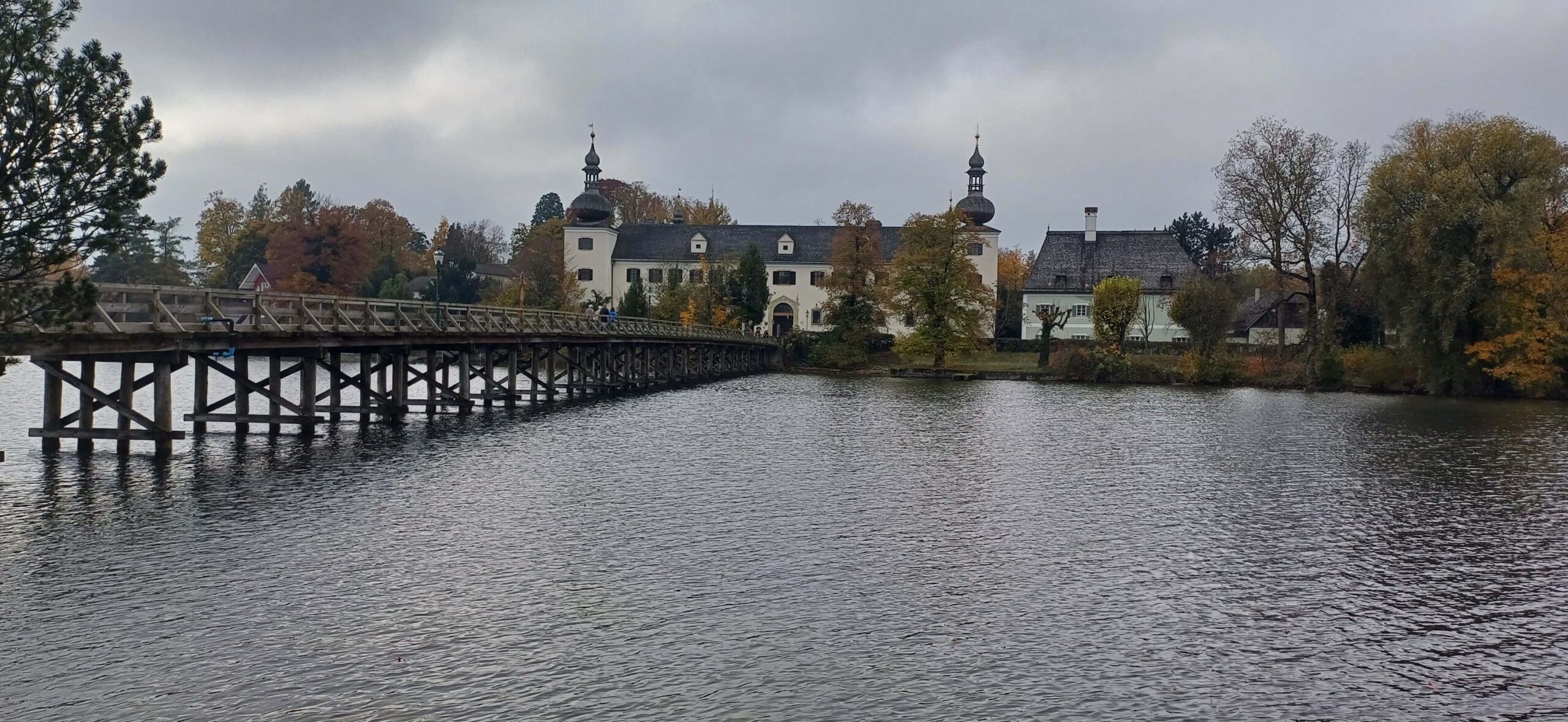 Zámek Ort, Gmunden: pohled na dřevěný most přes jezero Traunsee. Historická architektura a podzimní krajina.