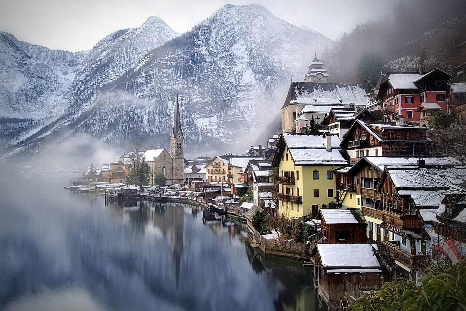 Hallstatt v zimě: zasněžené domy a kostel nad jezerem pod horami