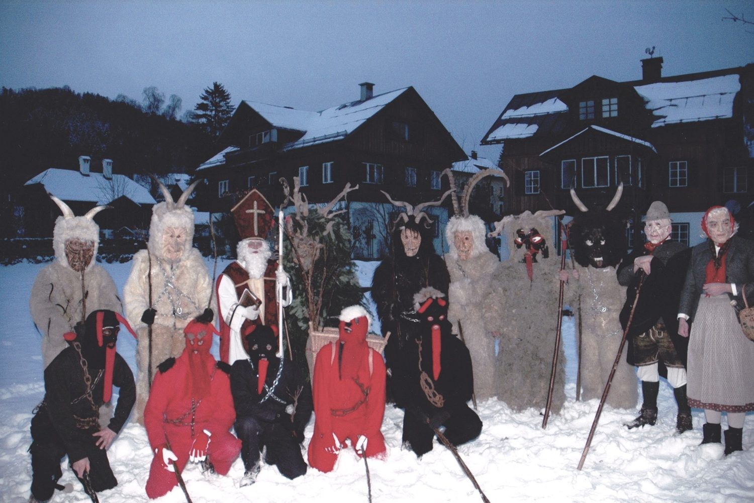 Skupina krampusů v tradičních maskách a kožešinách se svatým Mikulášem ve sněhu v Altaussee