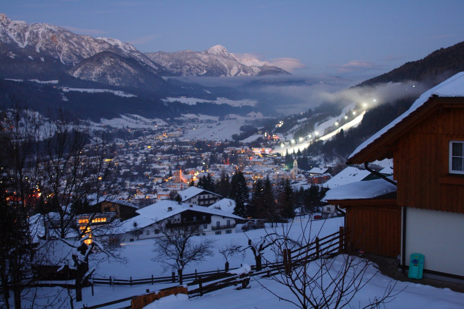 Schladming v prosinci za soumraku, zasněžené údolí se světly města a sjezdovkou Planai