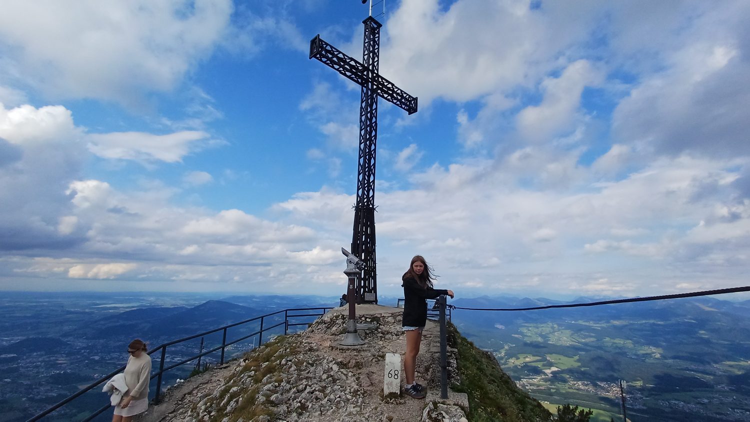 Vrcholový kříž na Untersbergu s dalekohledem na mince a zábradlím nad údolím