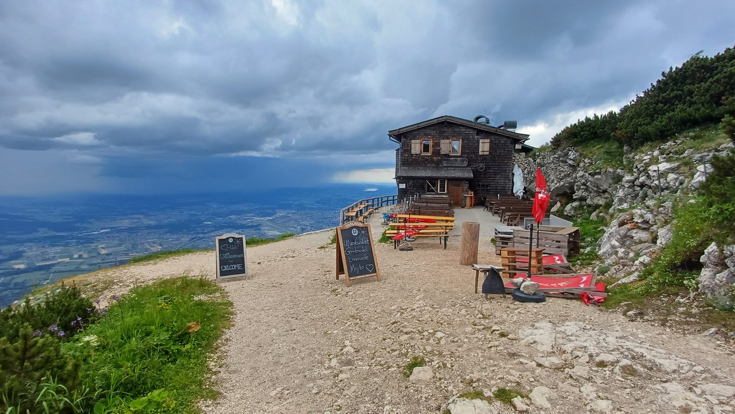 Horská chata s terasou na hraně srázu nad Salcburskem, nad rovinou bouřkové mraky a déšť