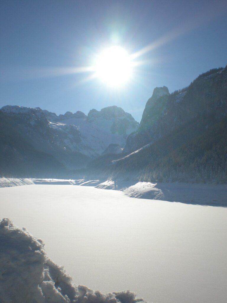 Zamrzlý a zasněžený Gosausee v zimním slunci, za ním Dachstein