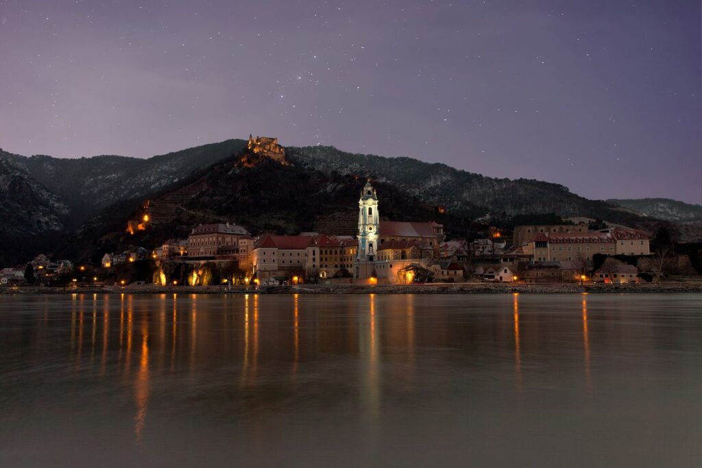 Dürnstein večer, osvětlená modrá věž klášterního kostela a zřícenina hradu nad Dunajem