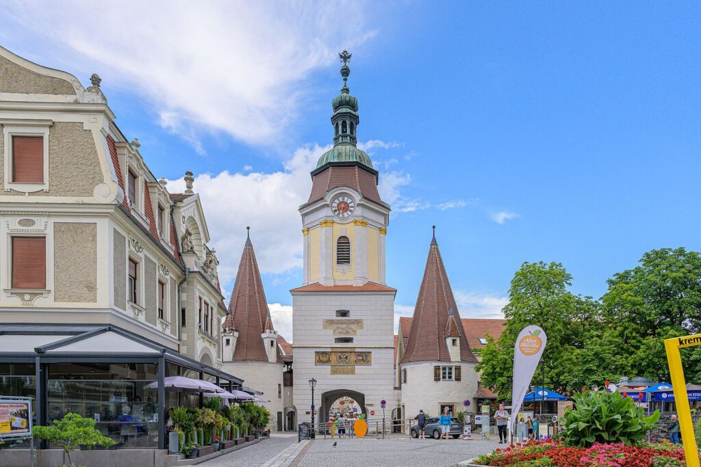 Steiner Tor v Kremsu, městská brána s věží a červenými střechami, vpravo květinový záhon