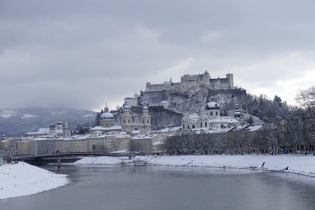 Zasněžené staré město Salcburku s pevností Hohensalzburg, pohled od řeky Salzach