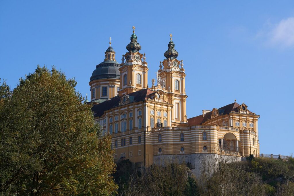 Barokní klášter Stift Melk se dvěma věžemi a kupolí nad stromy, v jasném podzimním světle